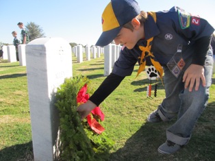 Young cub scout laying a wreath at a cemetary headstone