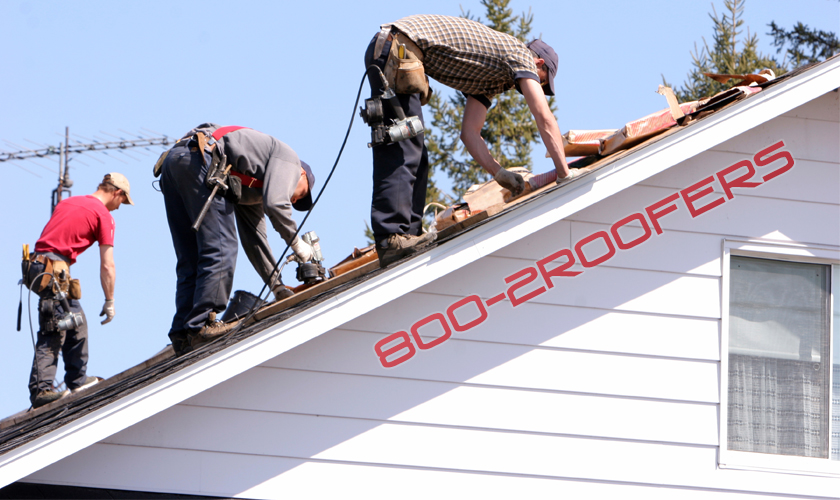 Three guys on a roof bent over working with 1-800-2ROOFERS on the house